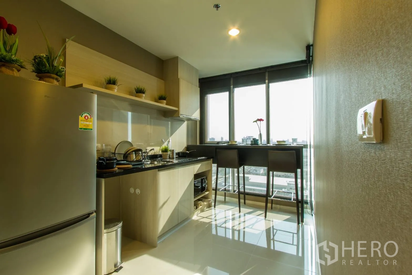 Condominium for rent or sale in Sathon, Bangkok - Modern kitchen with light-wood cabinetry, black countertop, stainless fridge and a city-view breakfast bar by wide windows.