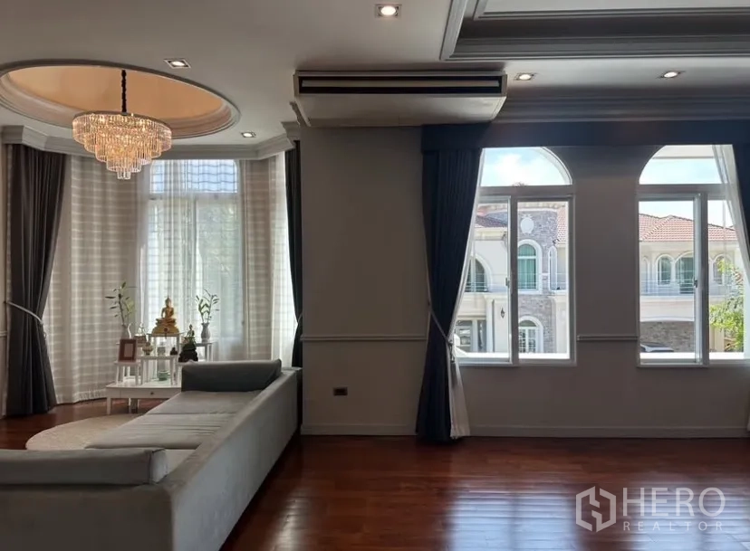 Detached House for rent or sale in Prawet, Bangkok - Bright upstairs lounge with crystal chandelier, bay windows, and arched windows overlooking the neighborhood.