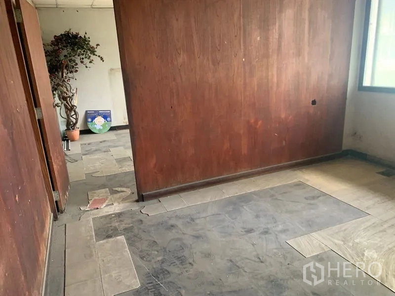 Shophouse for rent in Watthana, Bangkok - Compact room with wood panel wall, worn flooring and natural light from a window.
