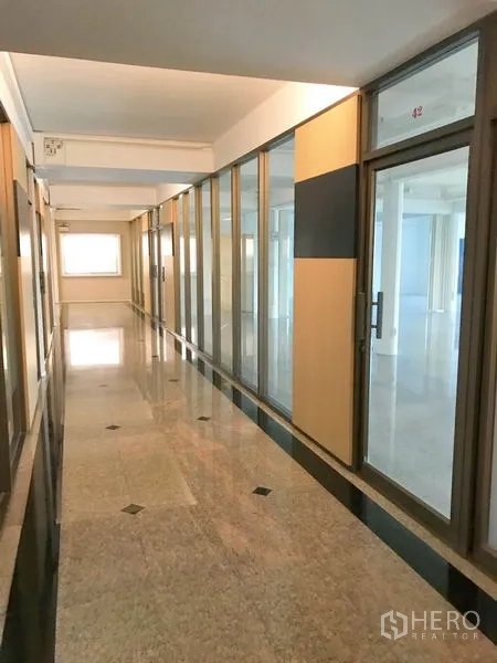 Office Space for rent in Suan Luang, Bangkok - Corridor with glass-partitioned office suites and reflective stone flooring.