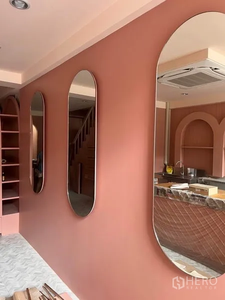 Shophouse for rent or sale in Watthana, Bangkok - Feature wall with oval mirrors beside staircase in a pink-toned interior.