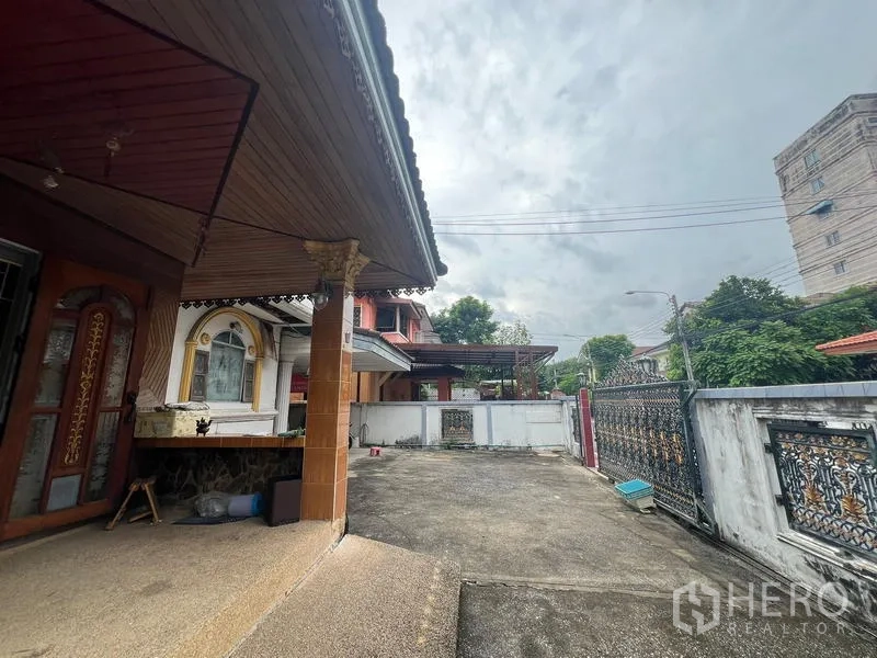 独立式住宅 出售在Phra Khanong, Bangkok - 前廊与宽阔车道，通向装饰性金属大门。