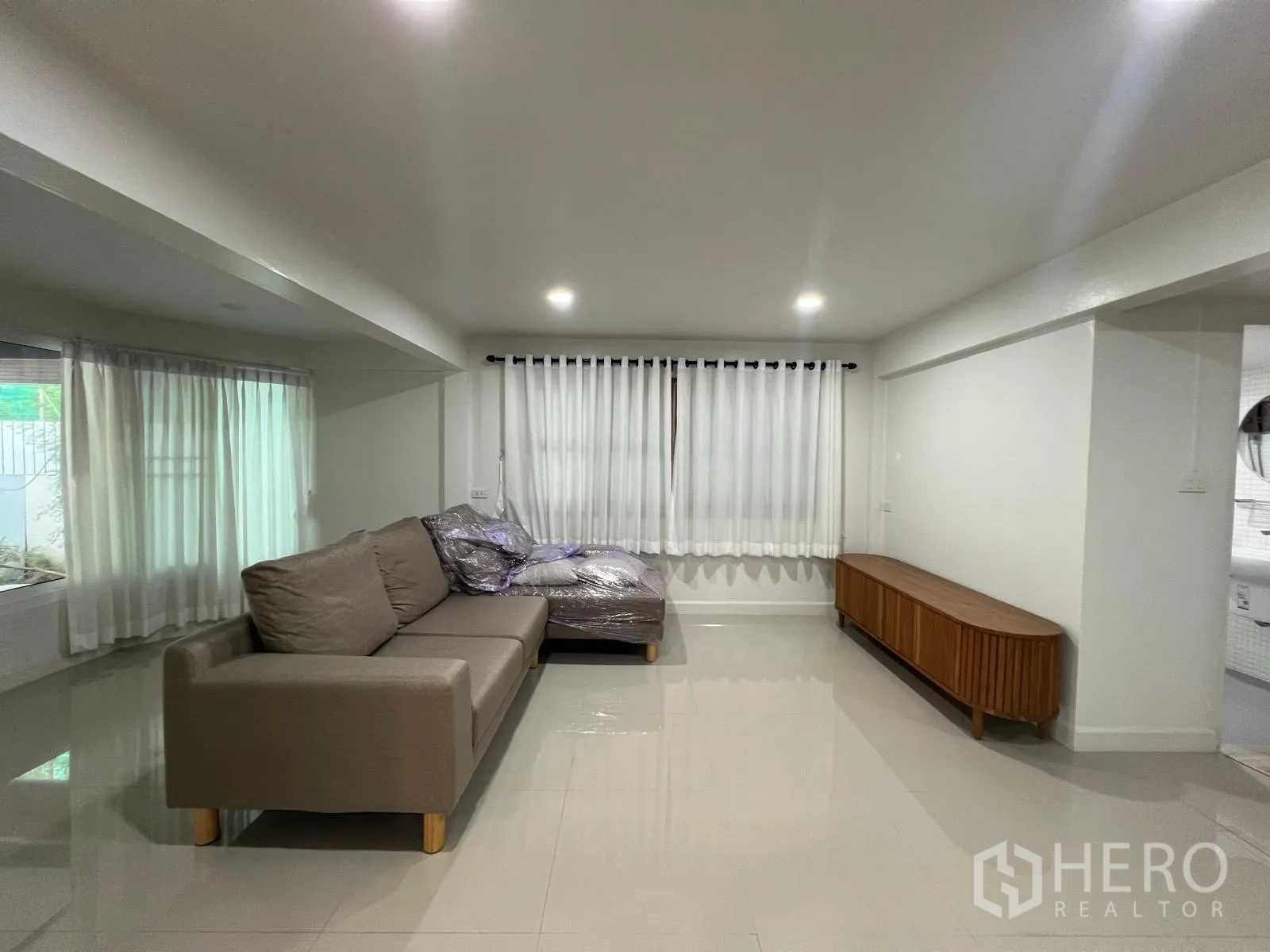 Detached House for rent in Saphan Sung, Bangkok - Living room with gray sofa, white curtains and a low wooden TV console.