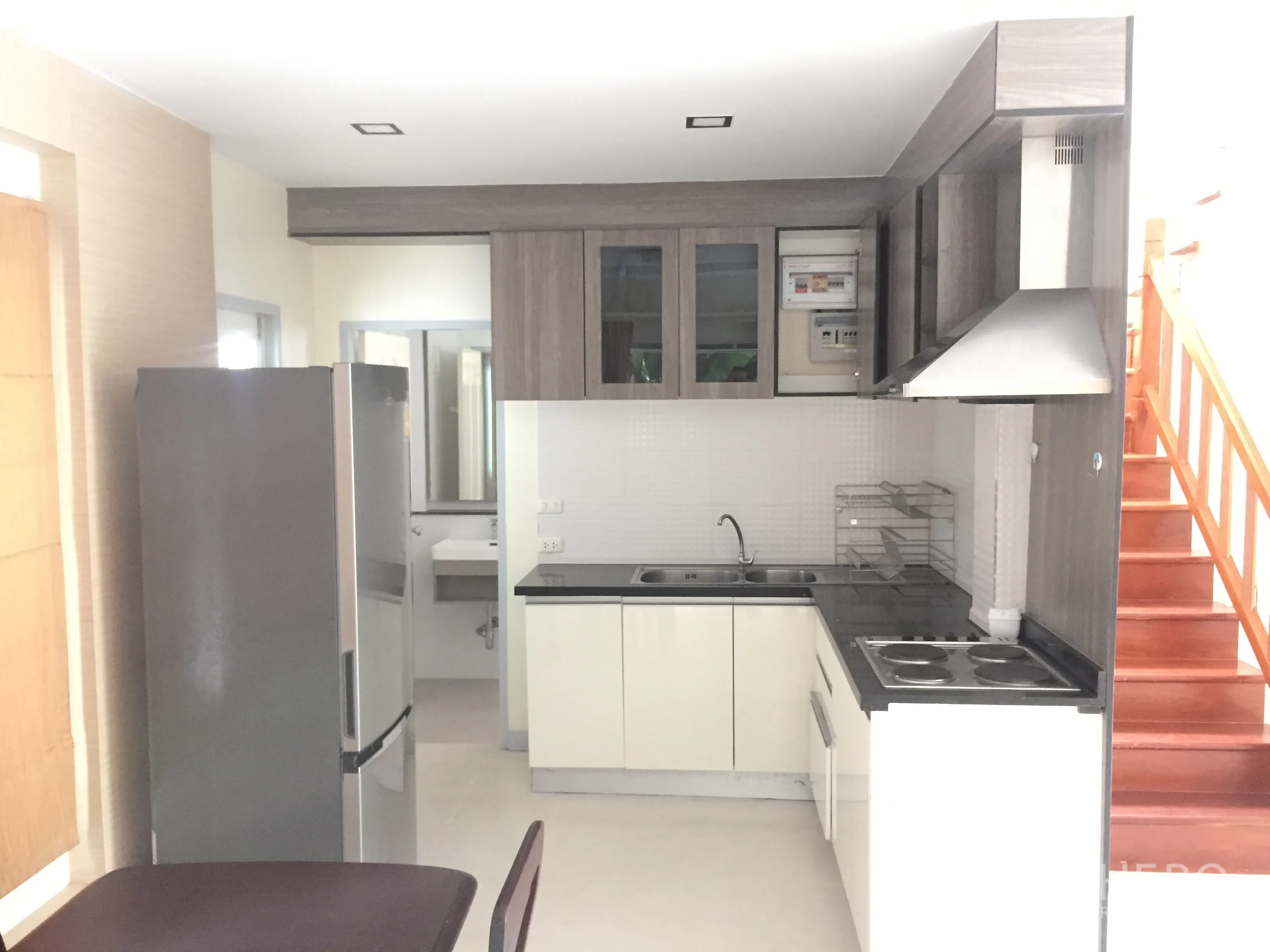 Detached House for sale in Lat Krabang, Bangkok - Compact modern kitchen with cabinets, cooktop, range hood and refrigerator beside the stairs.