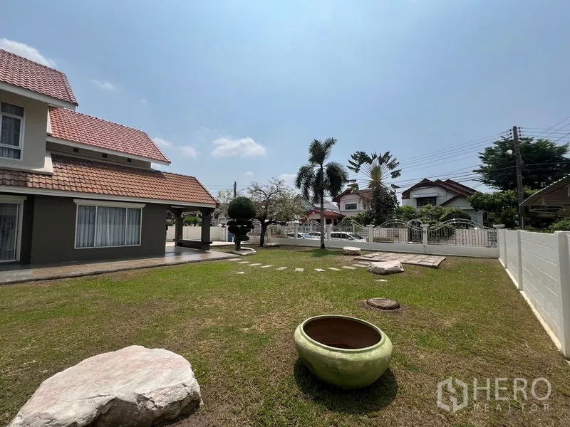 独立式住宅 出售在Mueang Pathum Thani, Pathum Thani - 宽阔草坪与房屋侧立面，大花盆与红瓦屋顶。