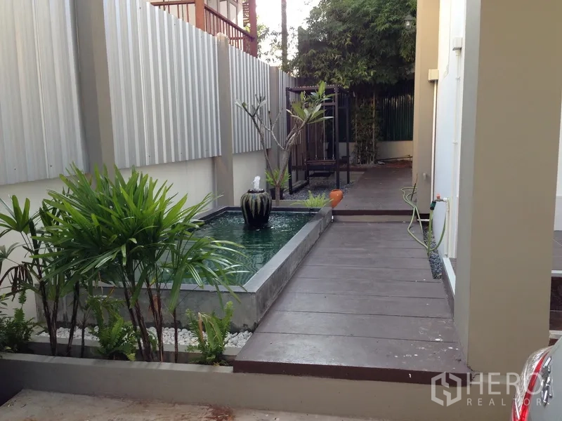 Detached House for sale in Phra Khanong, Bangkok - Side garden with a water feature pond, walkway and tropical plants for a serene corner.