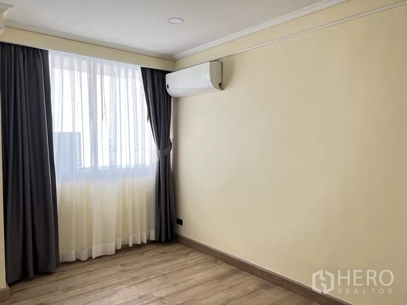 Condominium for rent in Khlong Toei, Bangkok - Empty secondary bedroom with large curtained window and wood-style flooring.