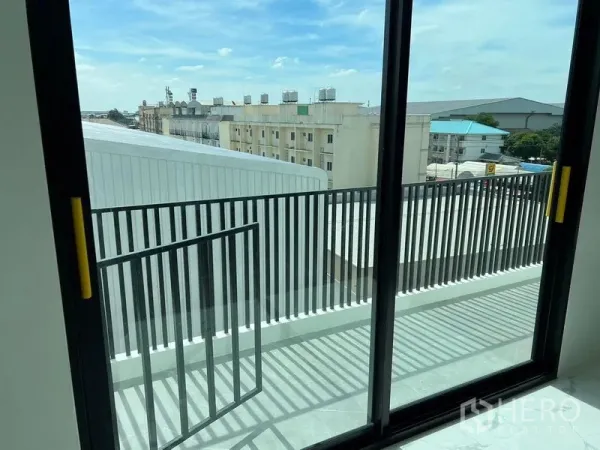Warehouse for rent in Bang Sao Thong, Samut Prakan - Balcony with black metal railing and sliding glass doors overlooking nearby industrial buildings.