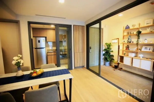 公寓 出租或出售在Watthana, Bangkok - 餐区设四人餐桌，可见配备不锈钢冰箱的独立厨房，并有通往阳光房的推拉门。