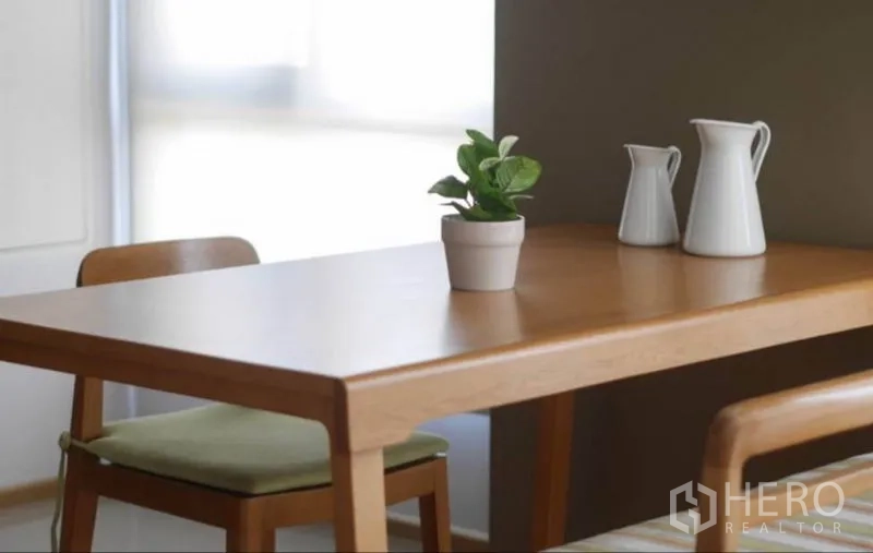 Condominium for rent in Phaya Thai, Bangkok - Close-up of wooden dining table with chairs, a small plant and ceramic jugs by a soft-lit window.