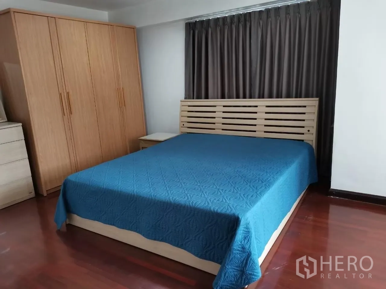 Condominium for rent in Phaya Thai, Bangkok - Bedroom with blue bedspread, wooden wardrobe, bedside tables and heavy curtains.