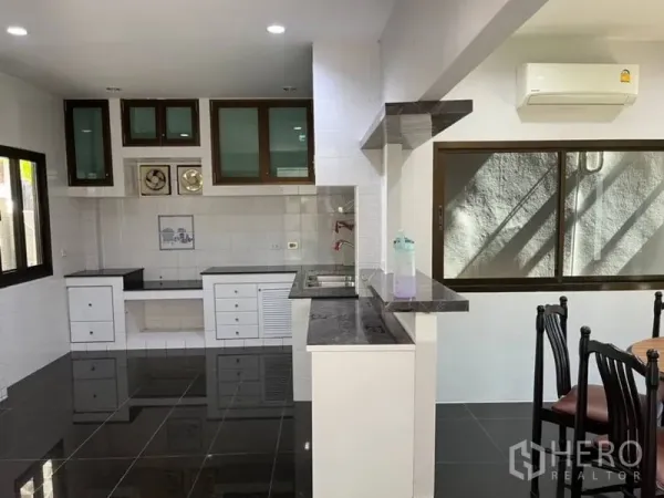 Detached House for rent in Samut Prakan - Open kitchen with black granite counters, white cabinets, and large windows.