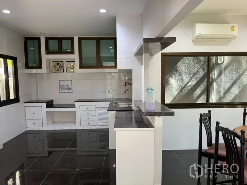 Detached House for rent in Samut Prakan - Open kitchen with black granite counters, white cabinets, and large windows.