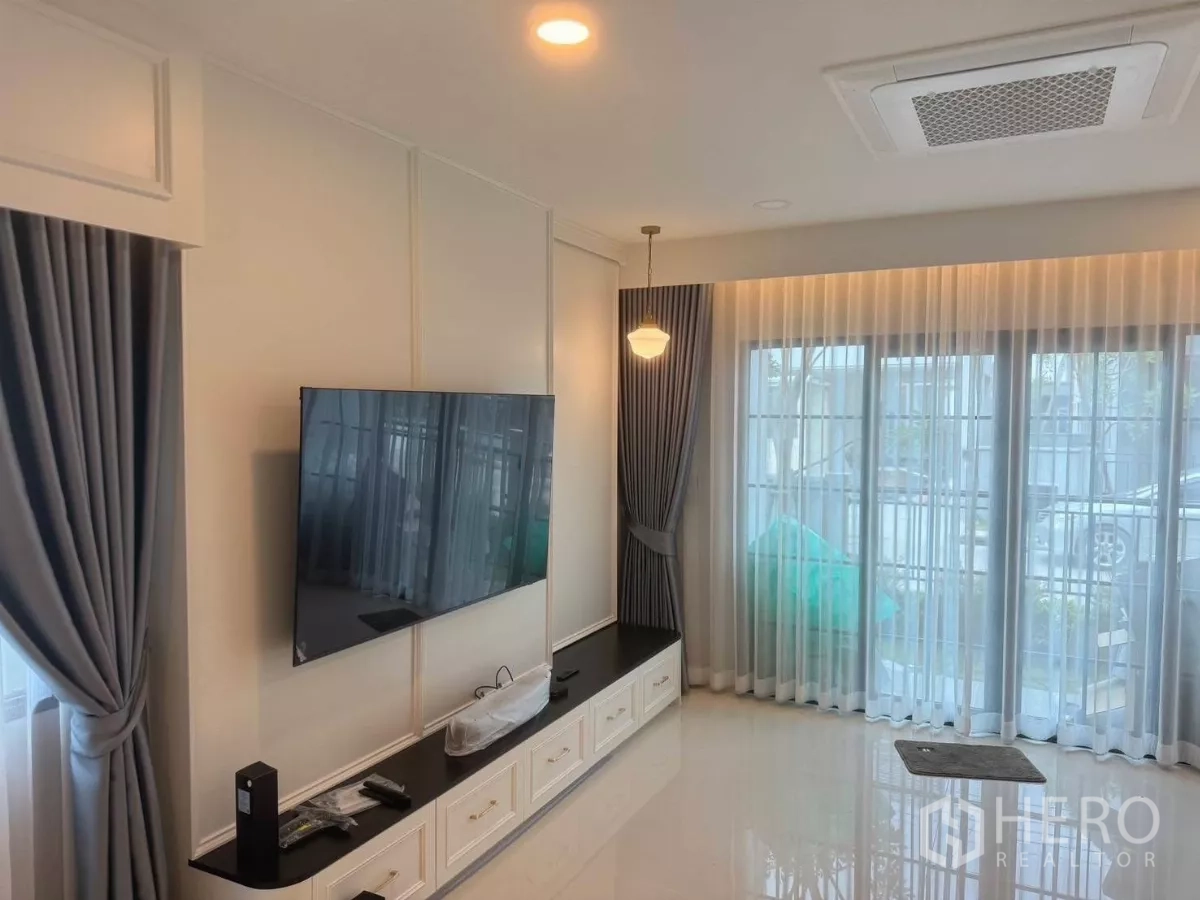 Detached House for rent in Bang Phli, Samut Prakan - Living room with wall-mounted TV, built-in console, ceiling cassette AC and floor-to-ceiling curtains.