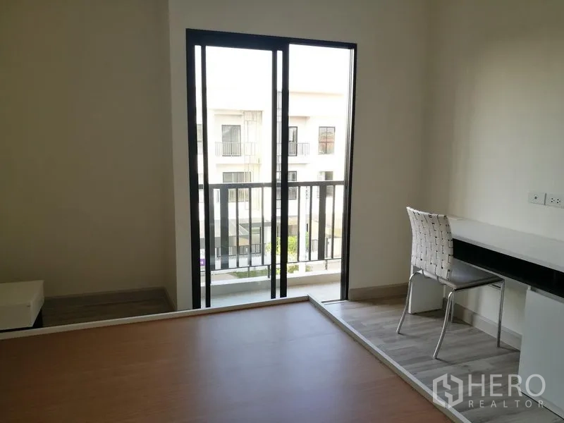 Townhouse for rent in Saphan Sung, Bangkok - Bedroom corner with desk, chair, and balcony view over the community.