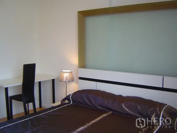 Condominium for rent in Chatuchak, Bangkok - Bedroom corner with study desk, modern headboard and bedside lamp.