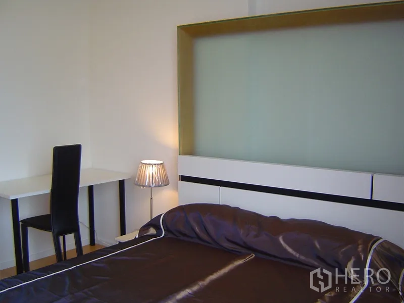 Condominium for rent in Chatuchak, Bangkok - Bedroom corner with study desk, modern headboard and bedside lamp.