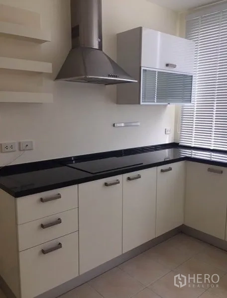 Condominium for rent in Watthana, Bangkok - Modern kitchen with cooktop, range hood and glossy black counters and drawers.