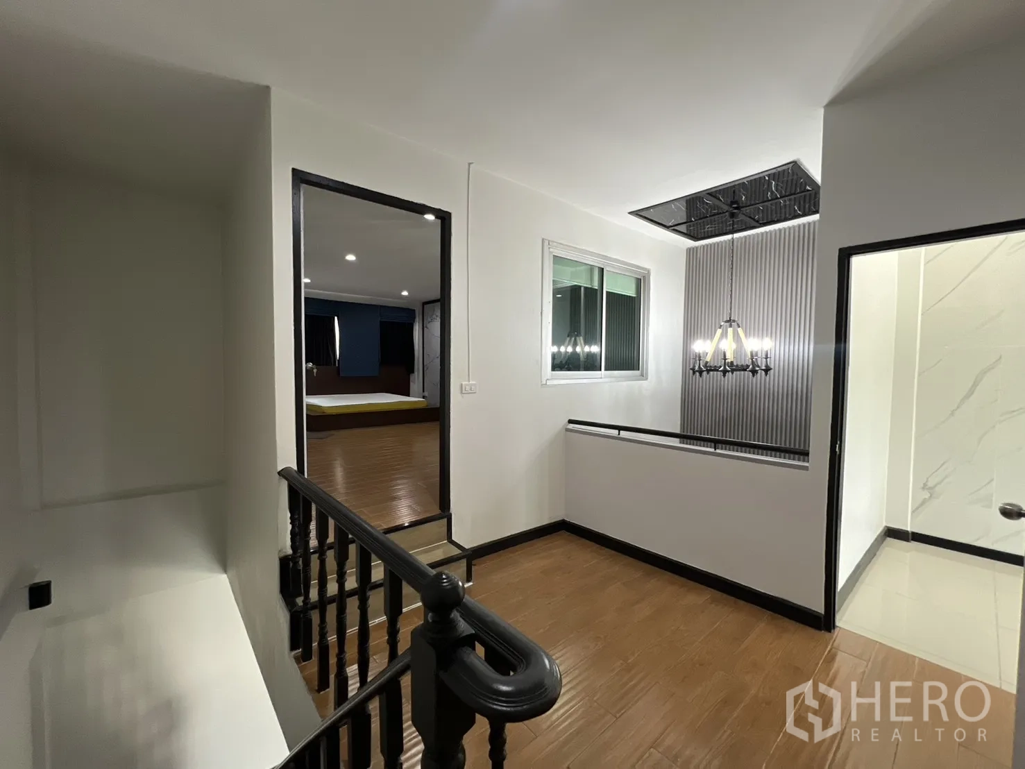 联排别墅 for rent in Watthana, Bangkok - 楼梯平台区，吊灯与木地板，可见卧室与浴室入口。