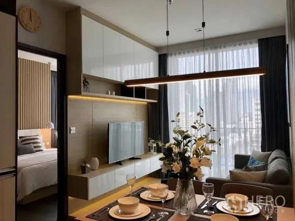 Condominium for rent in Watthana, Bangkok - Stylish living room with TV console, dining table and pendant light, with bedroom entrance visible.