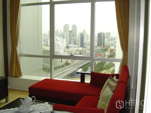 公寓 出租在Khlong San, Bangkok - 客厅红色贵妃沙发靠近大窗，可远眺曼谷城市与河景。