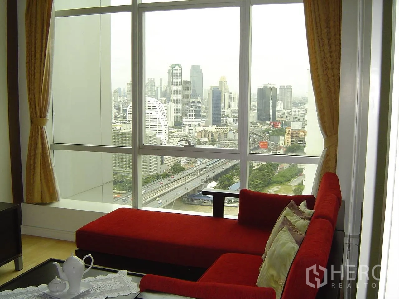 公寓 出租在Khlong San, Bangkok - 客厅红色贵妃沙发靠近大窗，可远眺曼谷城市与河景。