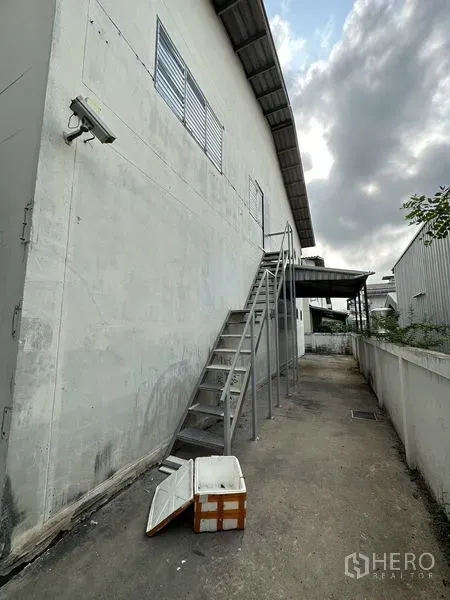 Factory for rent in Bang Bua Thong, Nonthaburi - External metal staircase along the warehouse wall providing service access.