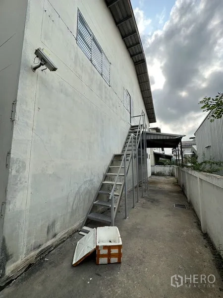 Factory for rent in Bang Bua Thong, Nonthaburi - External metal staircase along the warehouse wall providing service access.