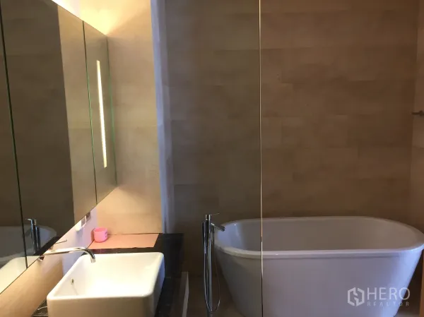 Condominium for rent or sale in Bang Rak, Bangkok - Bathroom featuring a freestanding bathtub, large mirror and square basin.