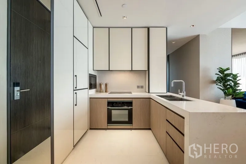Condominium for rent or sale in Khlong Toei, Bangkok - Modern L‑shaped kitchen with white cabinetry, built‑in oven and microwave, and peninsula sink.
