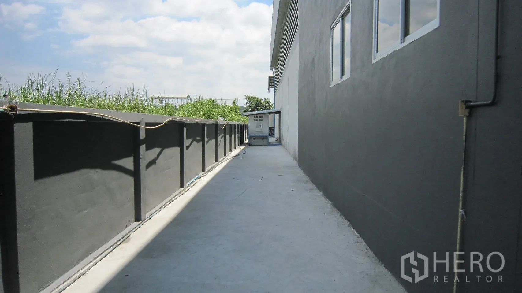 仓库 for rent in Bang Sao Thong, Samut Prakan - 仓库侧面混凝土通道，旁有围墙与设备箱。