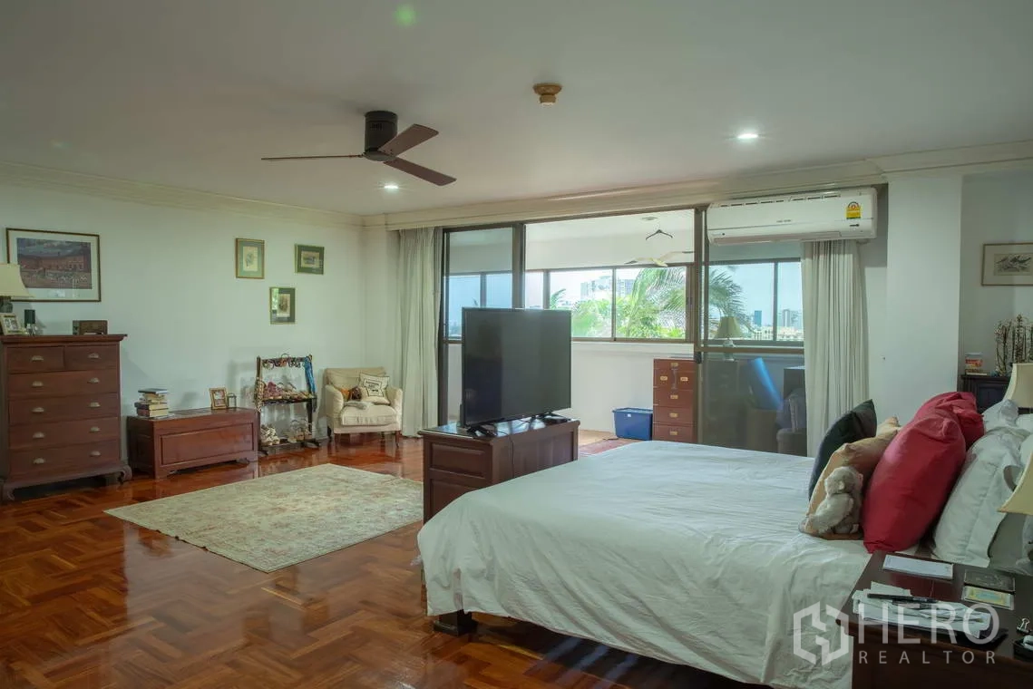 อพาร์ทเมนท์ for rent in Khlong Toei, Bangkok - ห้องนอนขนาดใหญ่พื้นปาร์เกต์ มีพัดลมเพดานและหน้าต่างเปิดสู่ระเบียง.