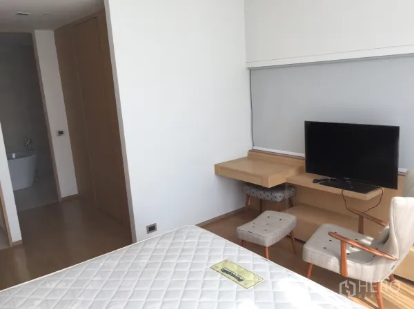 Condominium for rent in Bang Rak, Bangkok - Bedroom with built-in desk and TV, opening to an ensuite bathroom with soaking tub.