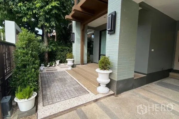 บ้าน ให้เช่าในSai Mai, Bangkok - ทางเข้าด้านหน้าบ้านพร้อมเฉลียง กระถางต้นไม้ และทางเดินปูพื้นสู่ที่จอดรถ
