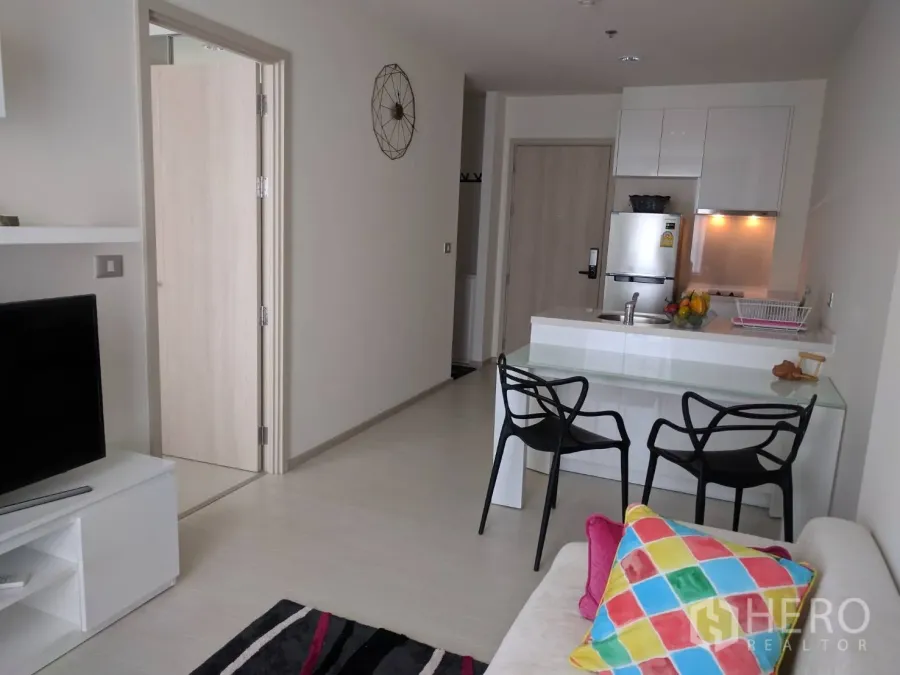 Condominium for rent in Khlong Toei, Bangkok - Open-plan living room with glass dining table, compact white kitchen, and TV console.