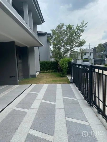 Detached House for rent or sale in Bang Kapi, Bangkok - Driveway area with small lawn and shade tree by the fence.