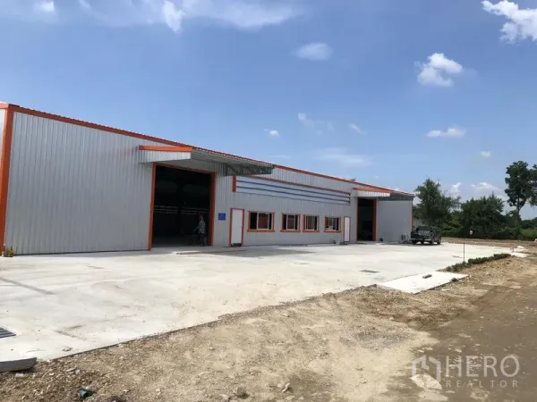 Warehouse for rent in Nonthaburi - Angled exterior view of a low-rise warehouse showing expansive driveway for truck maneuvering and multiple loading bays.