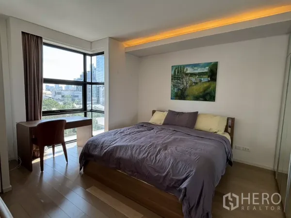 公寓 出售在Watthana, Bangkok - 转角卧室配大窗与双人床，书桌面向城市天际线。
