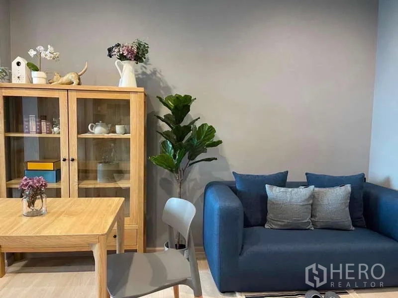 Condominium for rent in Pathum Wan, Bangkok - Cozy living corner with blue sofa, wooden display cabinet and indoor plant