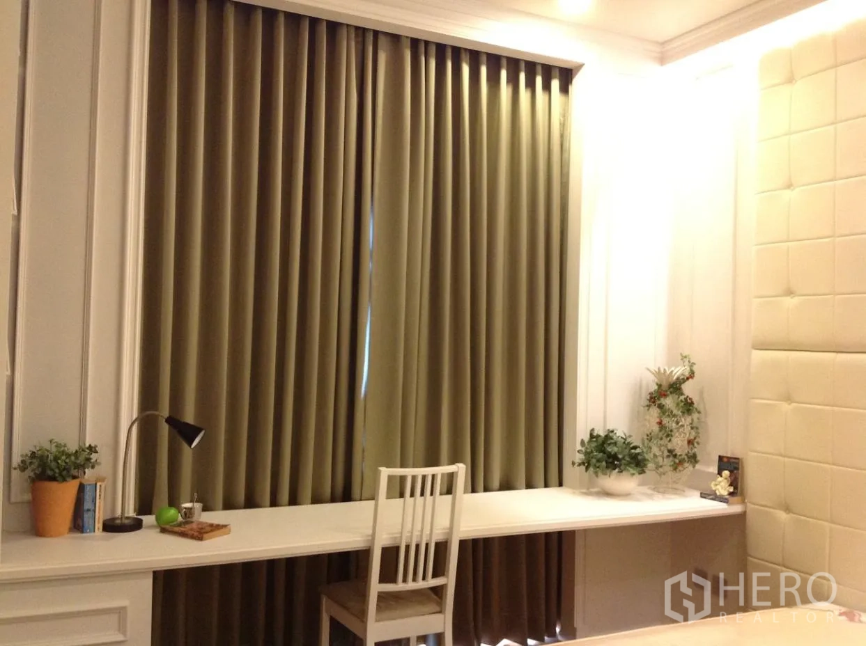 公寓 出租在Watthana, Bangkok - 卧室工作区配长条内置书桌、椅子、绿植与落地遮光窗帘。