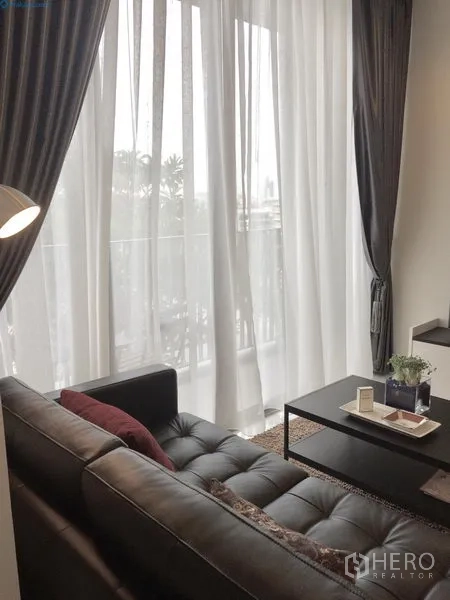 Condominium for rent or sale in Sathon, Bangkok - Cozy living room with tall curtains, coffee table, and balcony access through full-height glass doors.