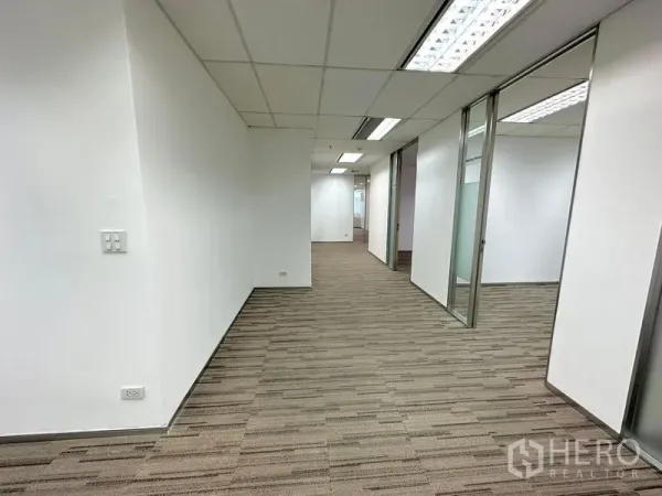 办公空间 出租在Watthana, Bangkok - 铺地毯的走廊，玻璃隔断办公室与推拉门，荧光灯照明。