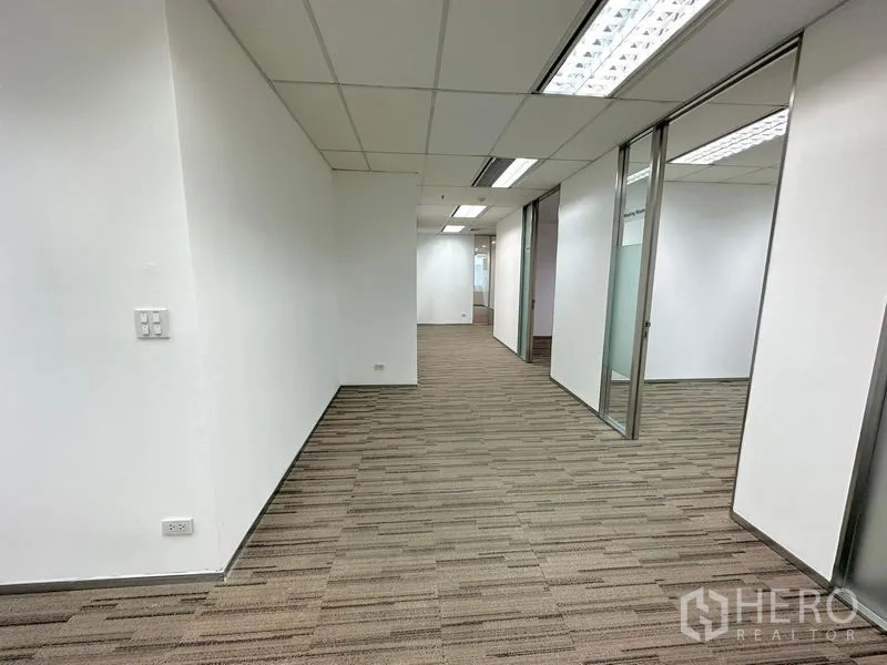 办公空间 出租在Watthana, Bangkok - 铺地毯的走廊，玻璃隔断办公室与推拉门，荧光灯照明。