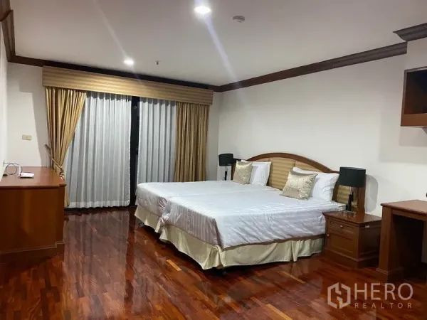 Condominium for rent in Watthana, Bangkok - Large master bedroom with king bed, polished wood flooring and full-length curtains.