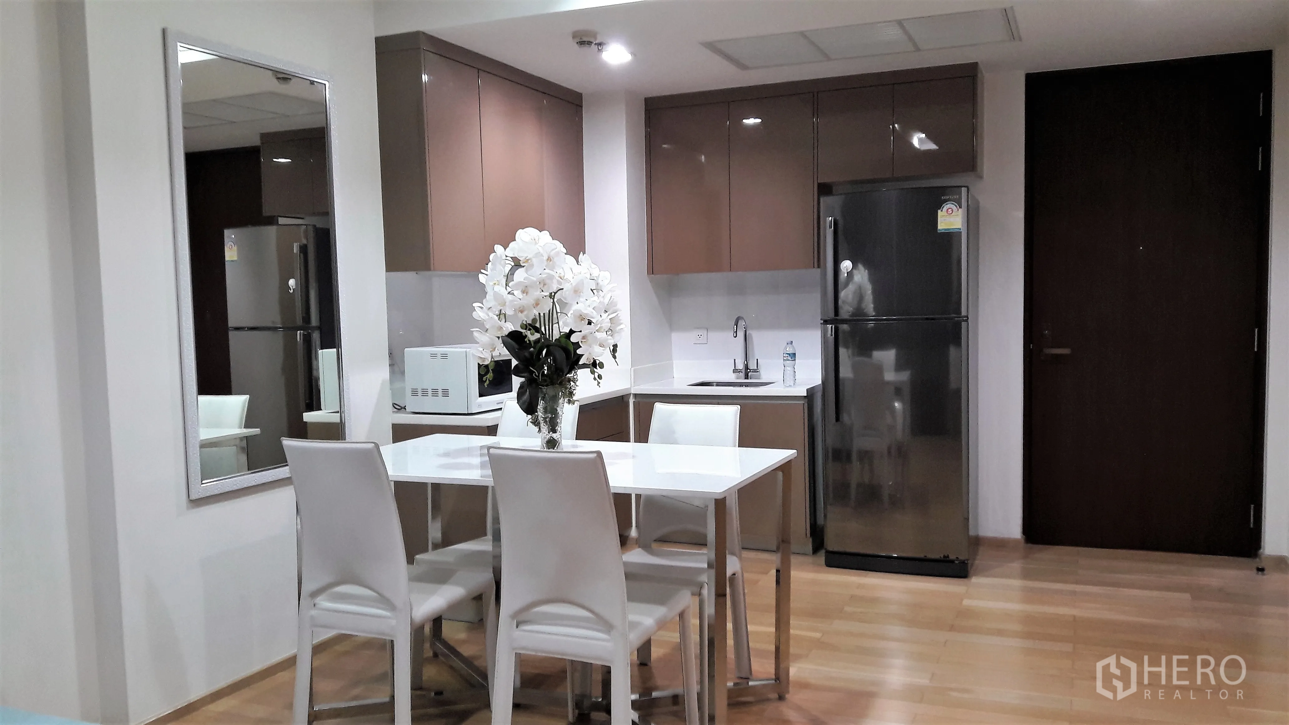 Condominium for rent in Khlong Toei, Bangkok - Open-plan kitchen and dining with glossy cabinets, full-size fridge, microwave and a white table for four.