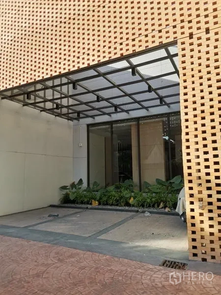 Retail Space for rent in Khlong Toei, Bangkok - Covered entrance of a modern retail building with glass storefront and planter beneath a perforated brick screen.