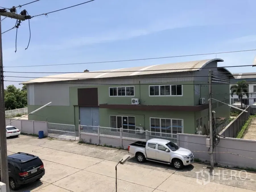 Factory for rent in Pathum Thani - Two-storey green factory with gated fence and roller door viewed from the street.