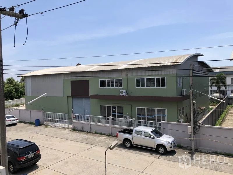 Factory for rent in Pathum Thani - Two-storey green factory with gated fence and roller door viewed from the street.