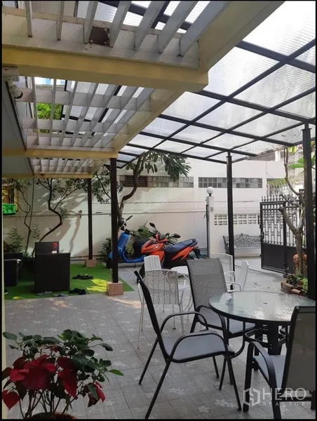 บ้าน ให้เช่าในWatthana, Bangkok - เฉลียงมีหลังคาใส โต๊ะนั่งเล่นกลางแจ้ง และมอเตอร์ไซค์จอดข้างสนามหญ้า