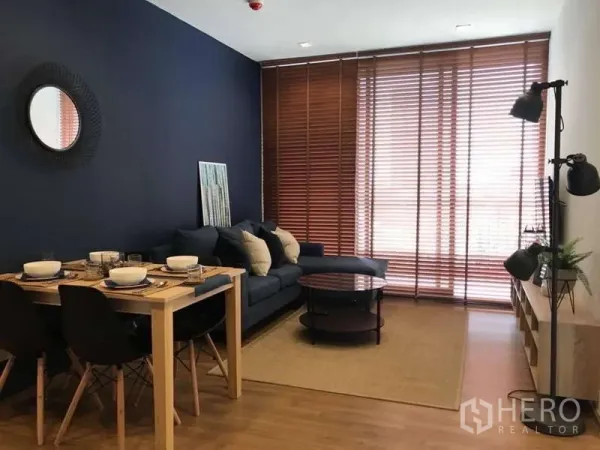 公寓 出租在Watthana, Bangkok - 海军蓝特色墙的客餐厅，沙发与木百叶窗。